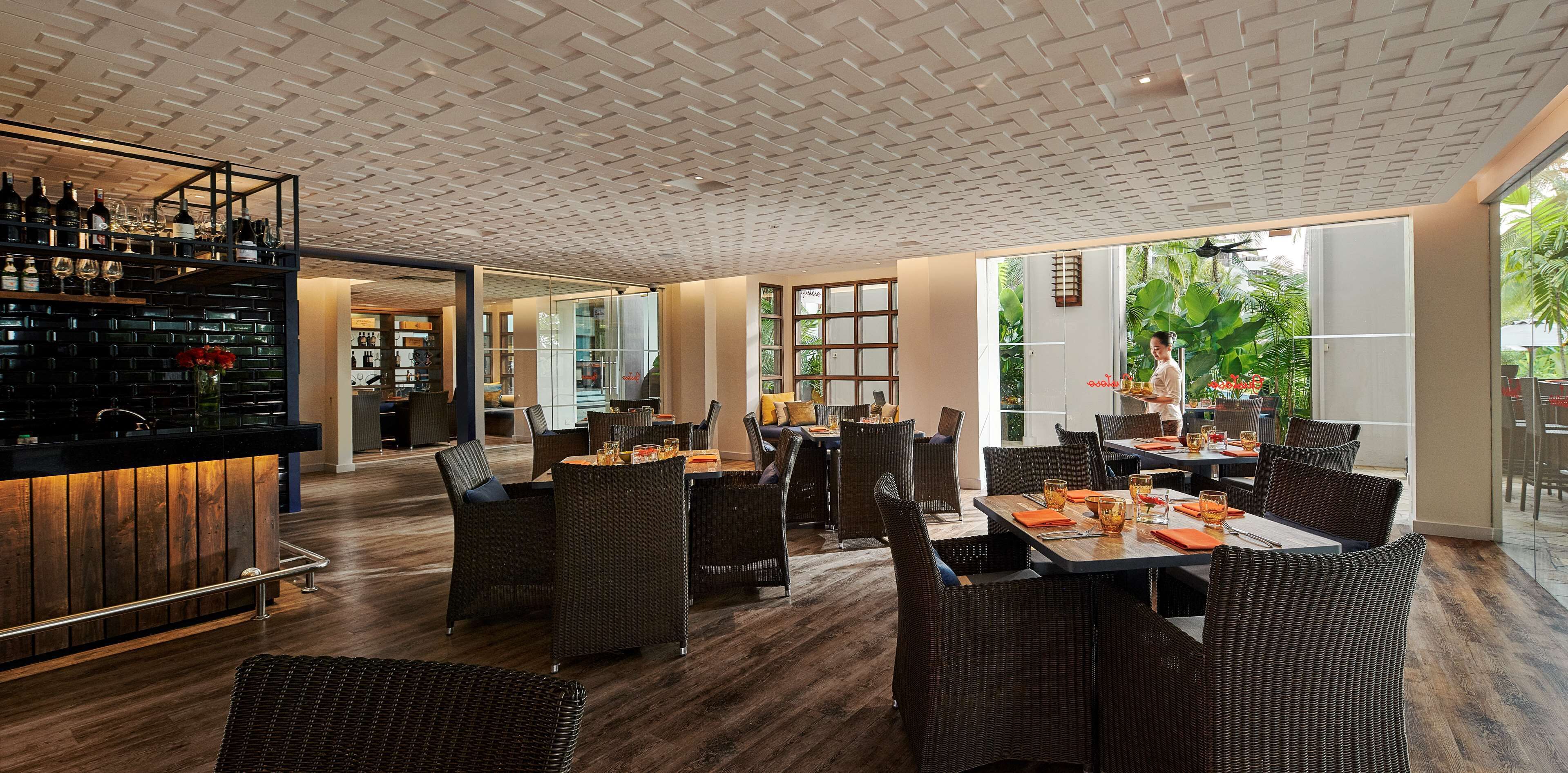 A restaurant with wicker furniture, a bar area, and large windows offering a view of the outdoors.