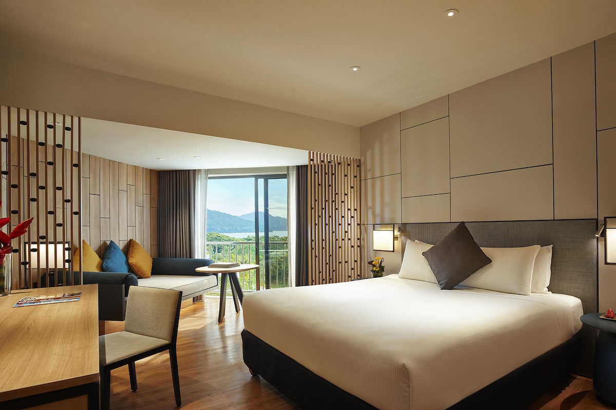 A modern hotel room with a large bed, a dining table, and a balcony with a view of the mountains.