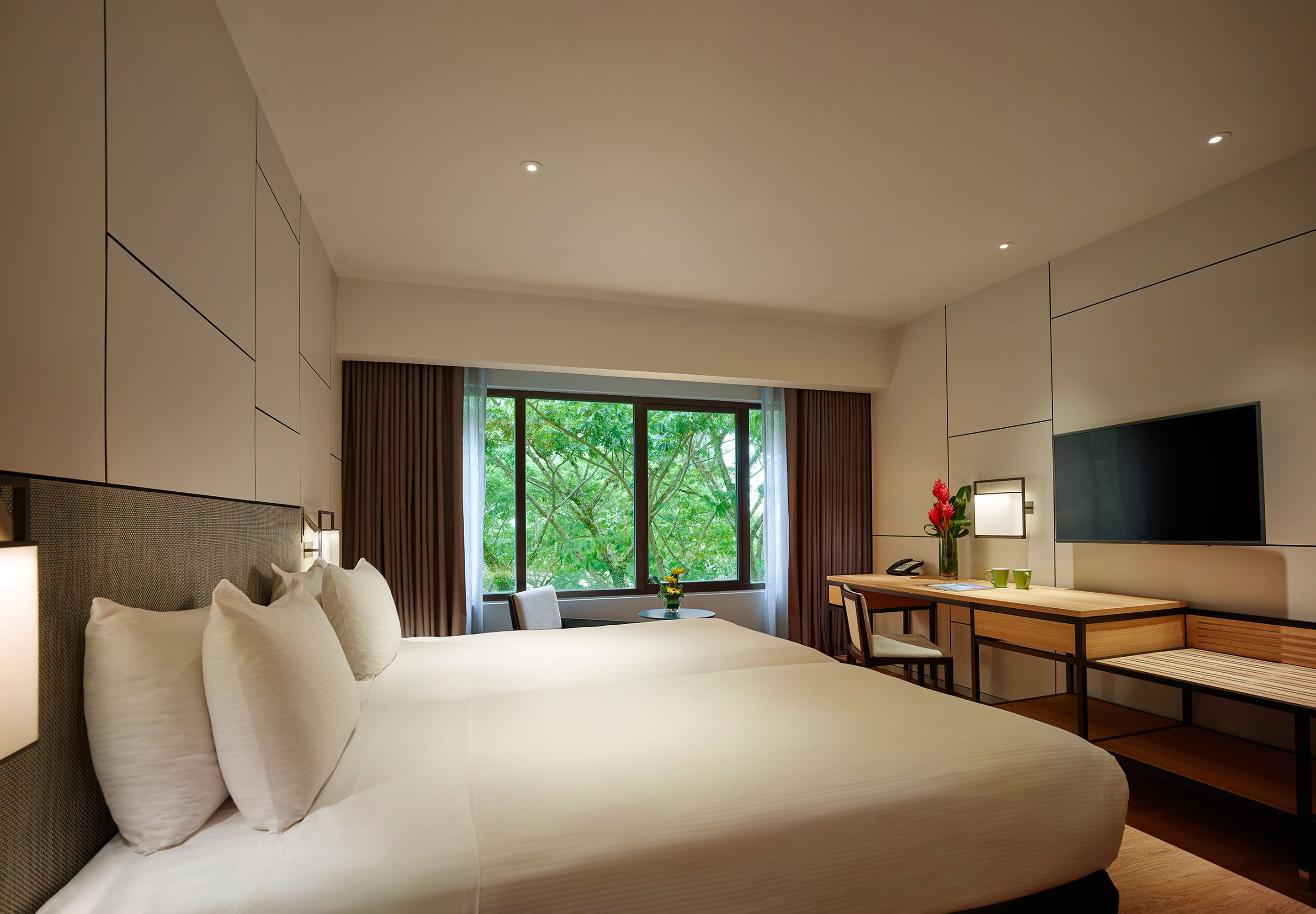 A modern hotel room with a large bed, a desk, a chair, and a TV.