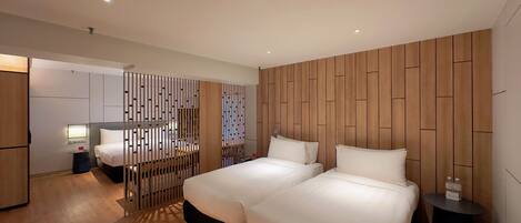 A modern hotel room with two beds, a wooden panel wall, a small bedside table, and a desk with a chair.