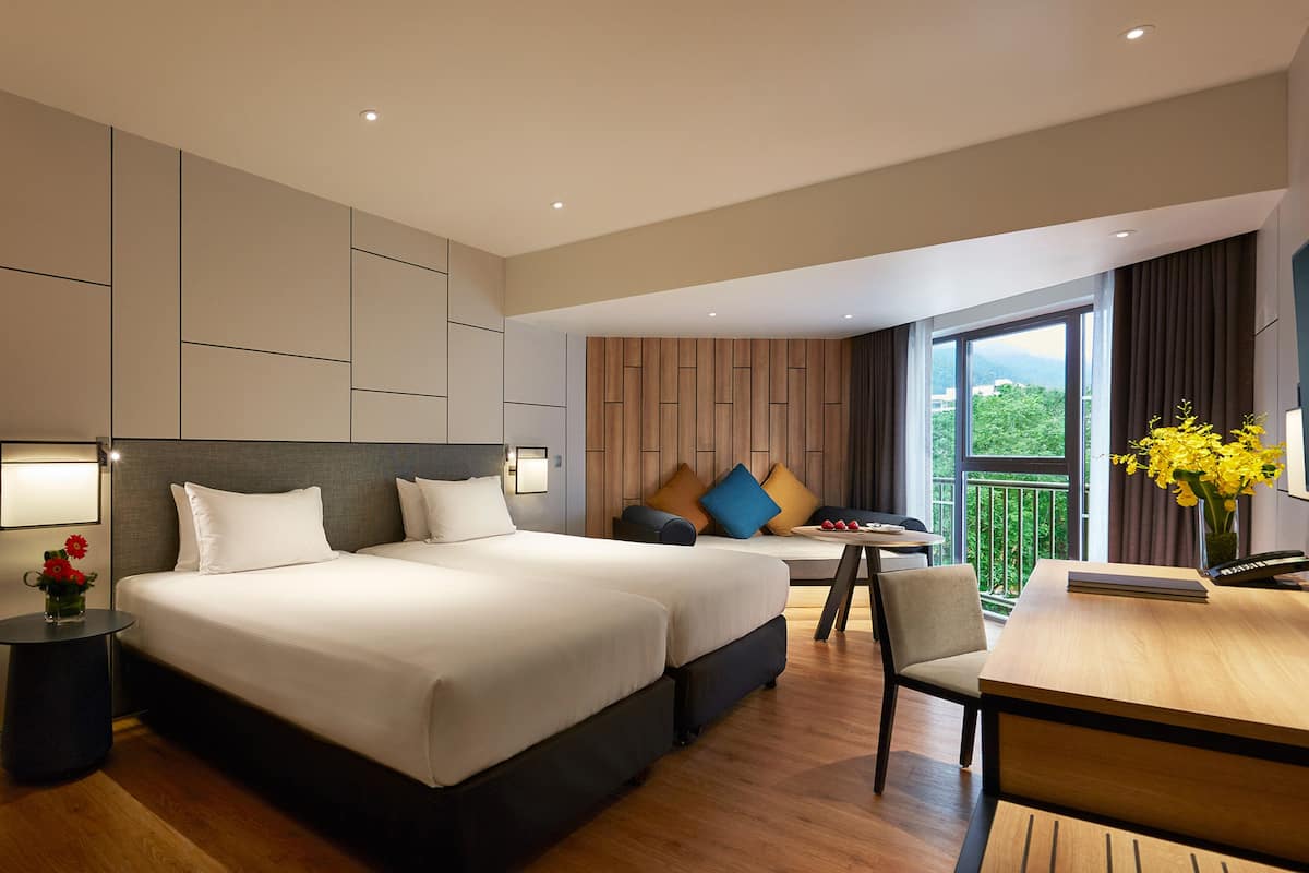 A modern hotel room with two beds, a desk, and a balcony with a view.