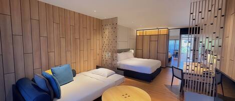 Una habitación de hotel moderna con un panel de pared de madera, un sofá con cojines azules, una cama, una mesa redonda de madera y un balcón con barandilla.