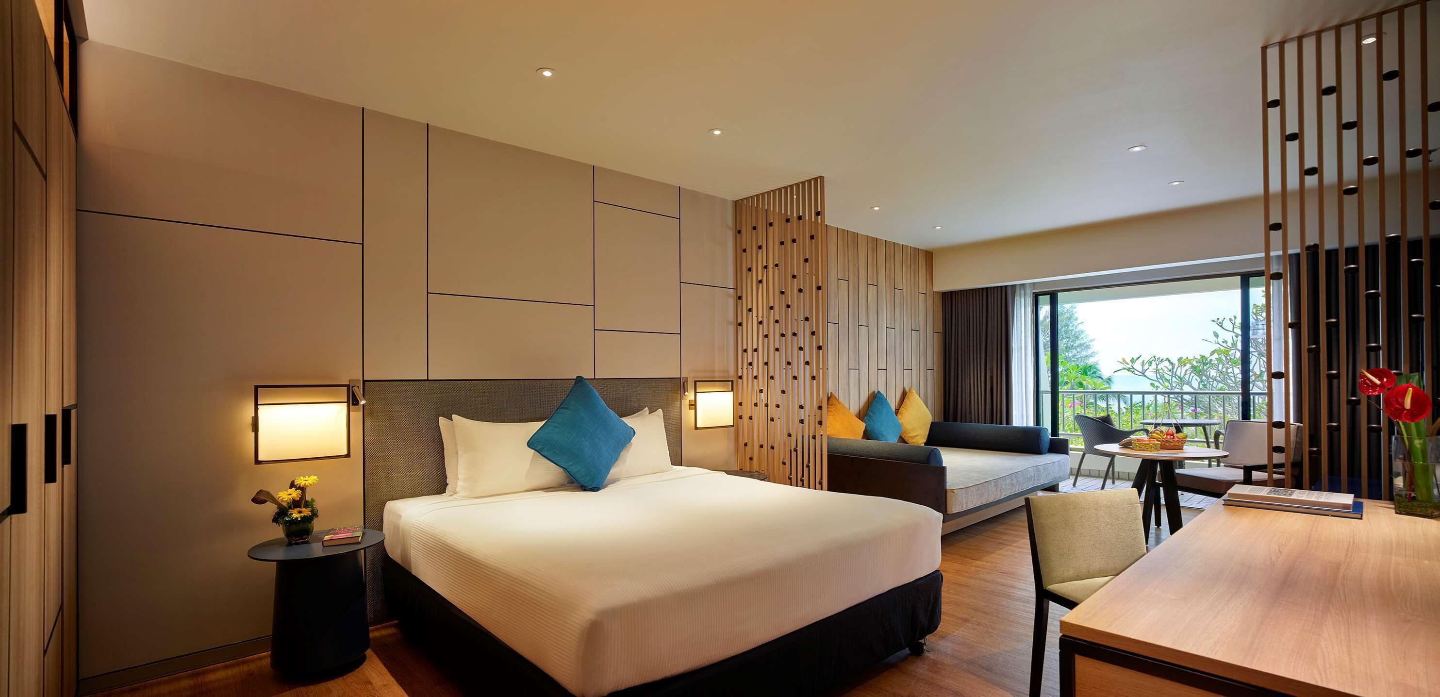 A modern hotel room with a large bed, a sofa, a desk, and a balcony with a view.