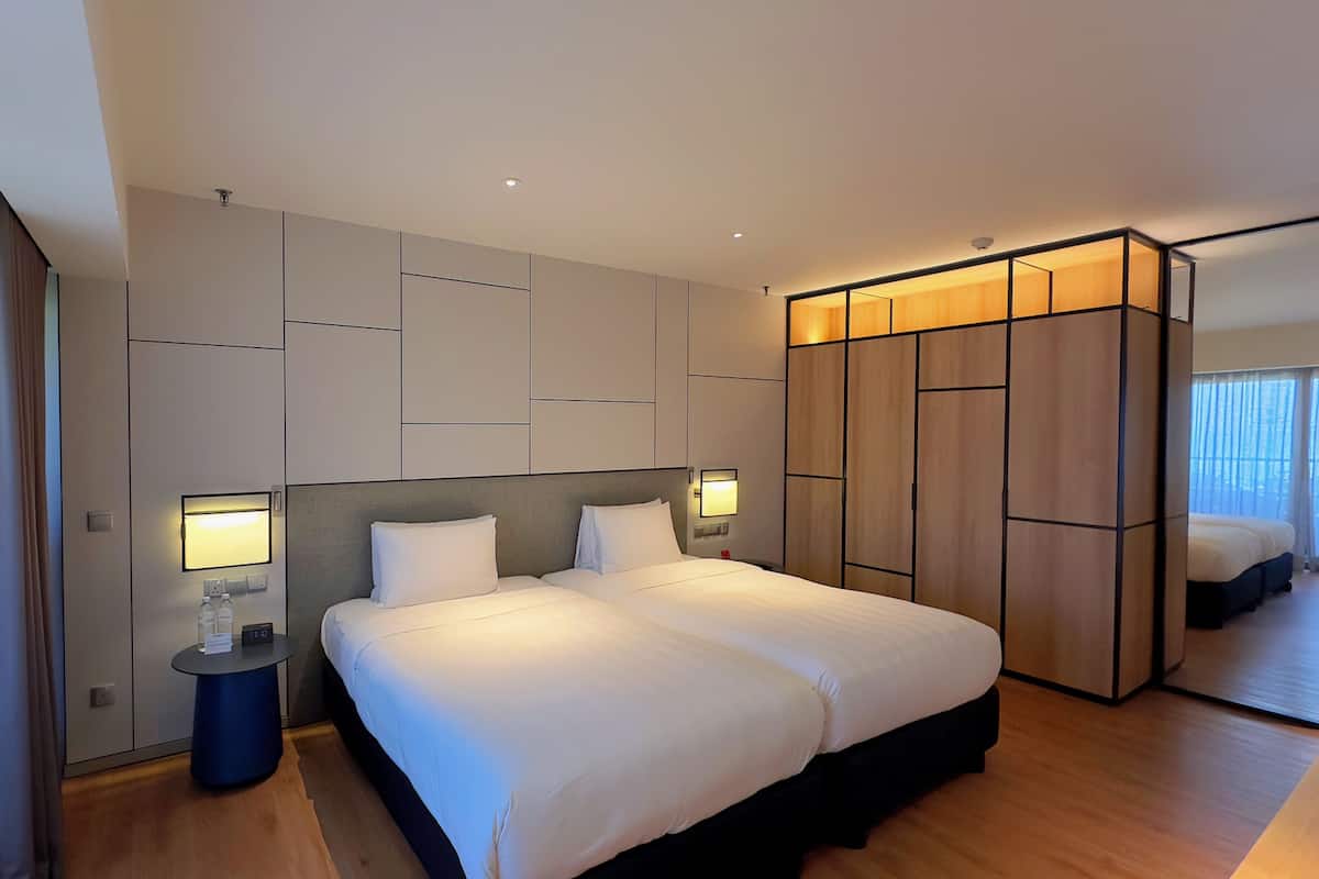 A modern hotel room with a large bed, a bedside table, a wardrobe, and a view of the balcony.