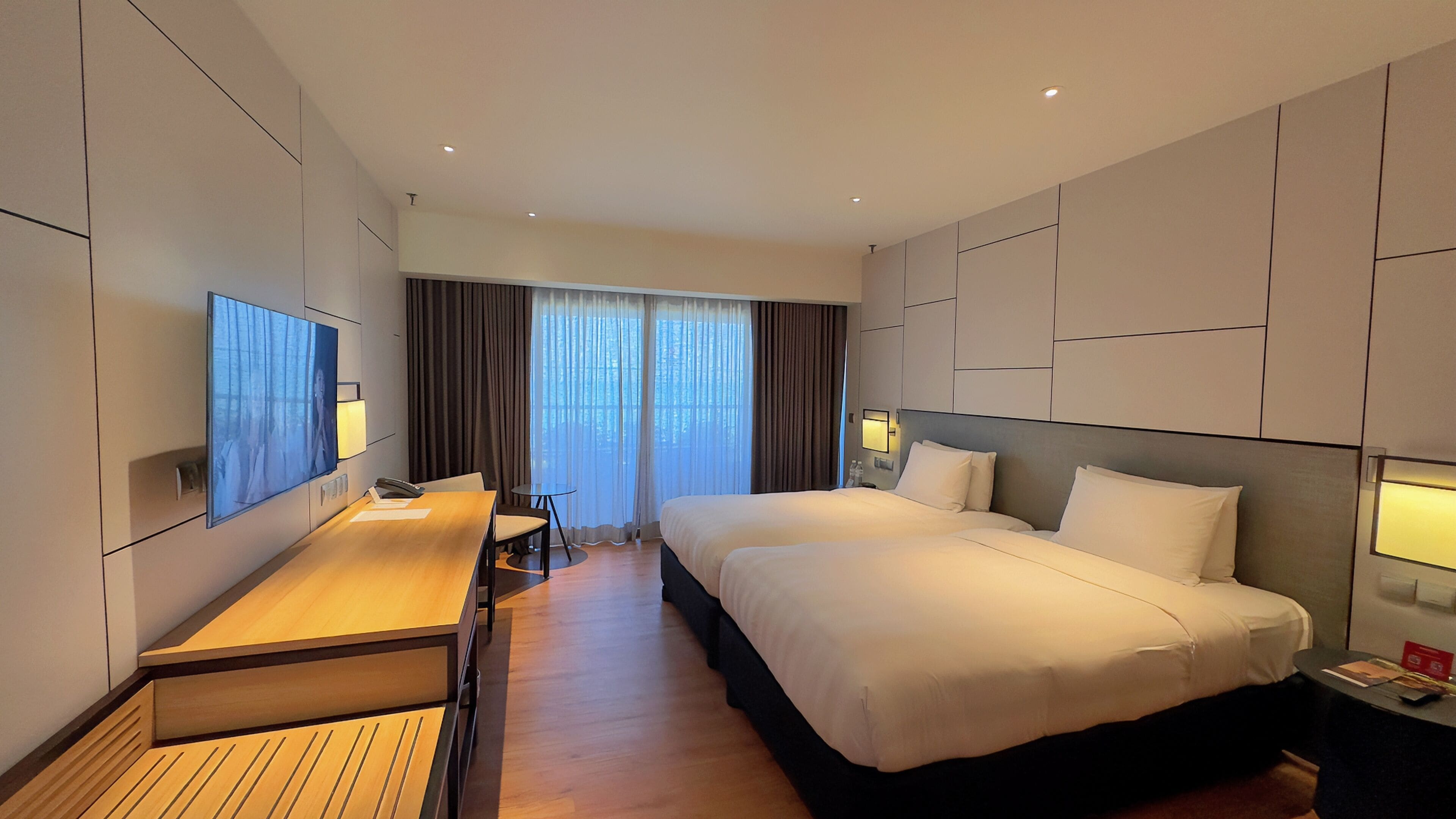 A modern hotel room with a large bed, a desk, and a TV mounted on the wall.