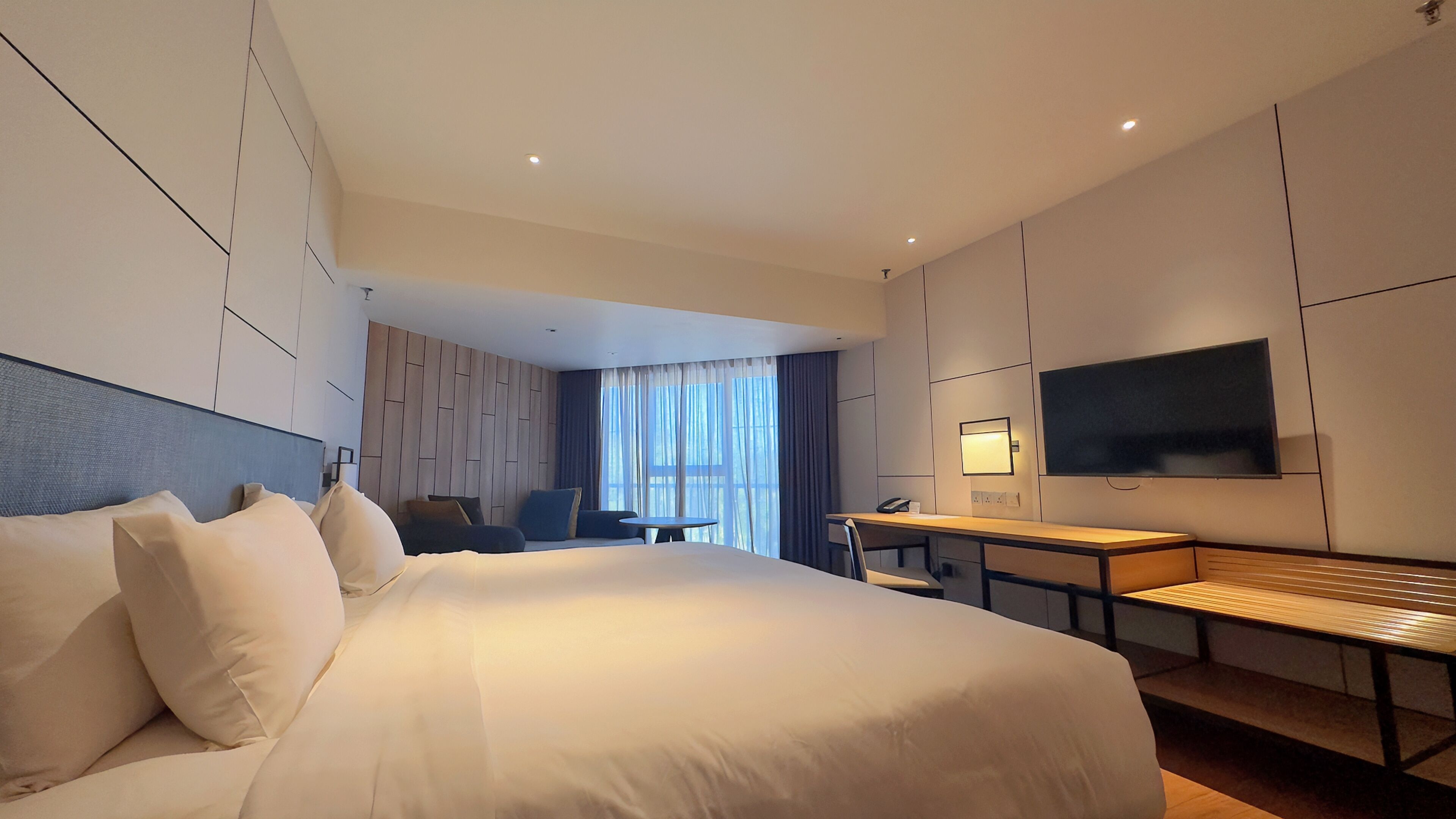 Une chambre d’hôtel moderne équipée d’un grand lit, d’un bureau, d’une chaise, d’une télévision et d’une fenêtre avec des rideaux.