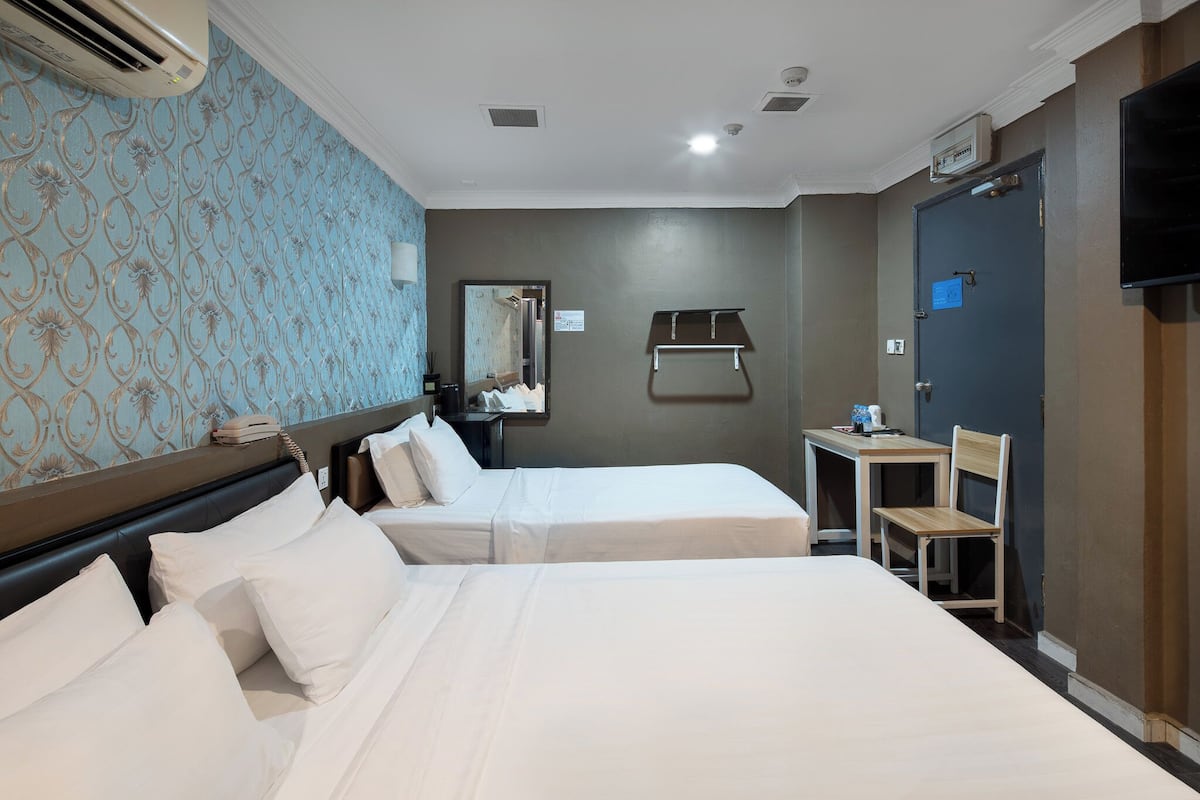 A hotel room with two beds, a desk with a chair, a mirror, and a TV mounted on the wall.