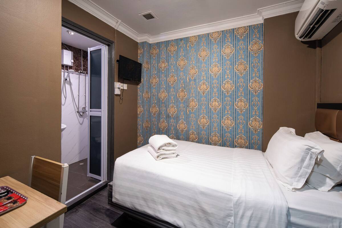 A hotel room with a bed, a desk, and a shower area.
