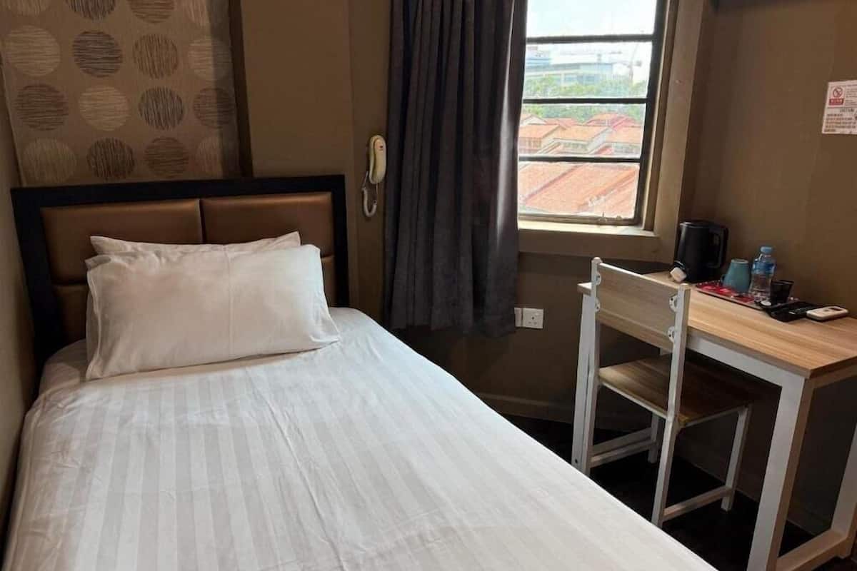 A hotel room with a bed, a desk, a chair, a telephone, and a window with a view of buildings.