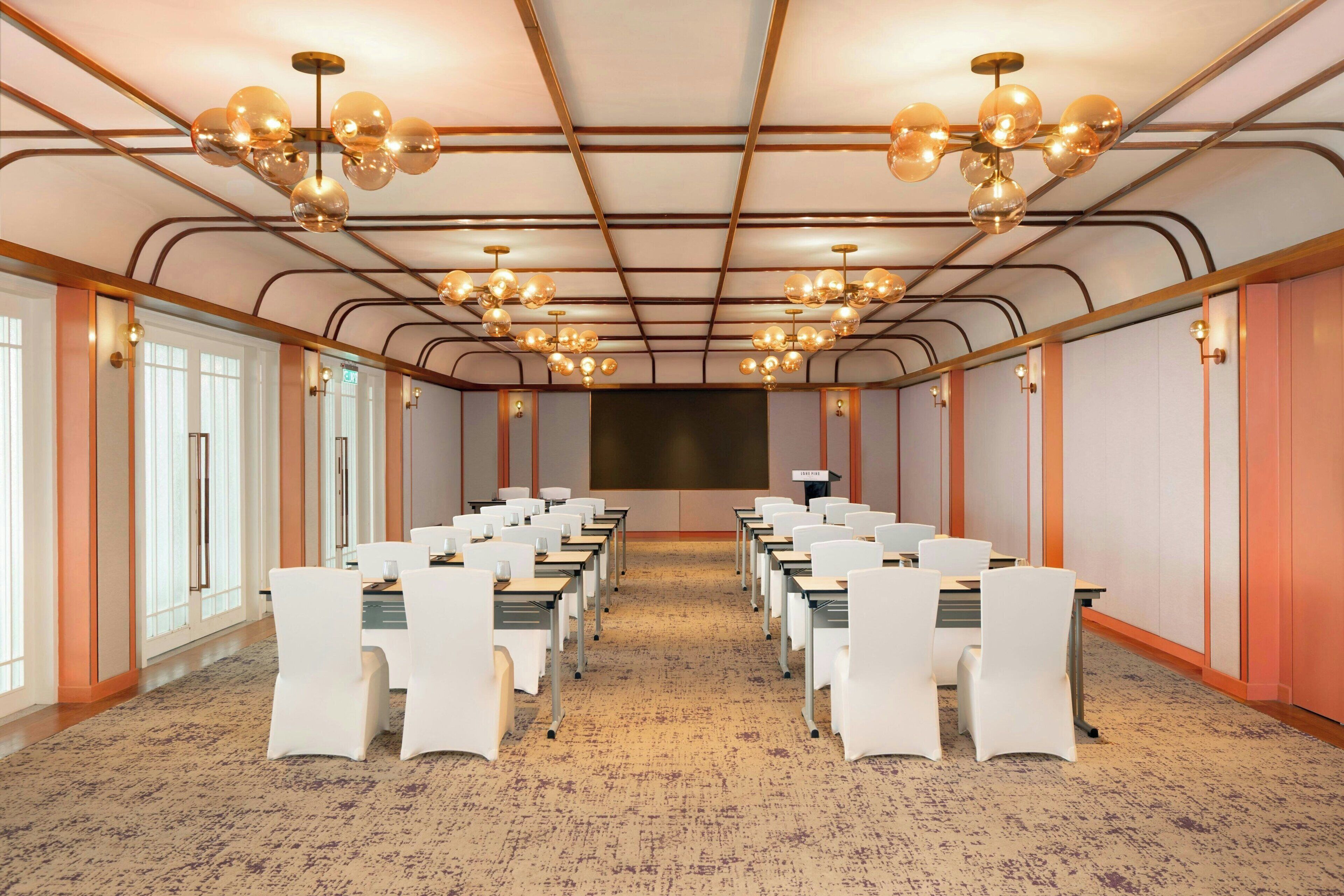 Une salle de conférence avec des rangées de chaises blanches, un sol recouvert de moquette et un grand écran à l’avant.
