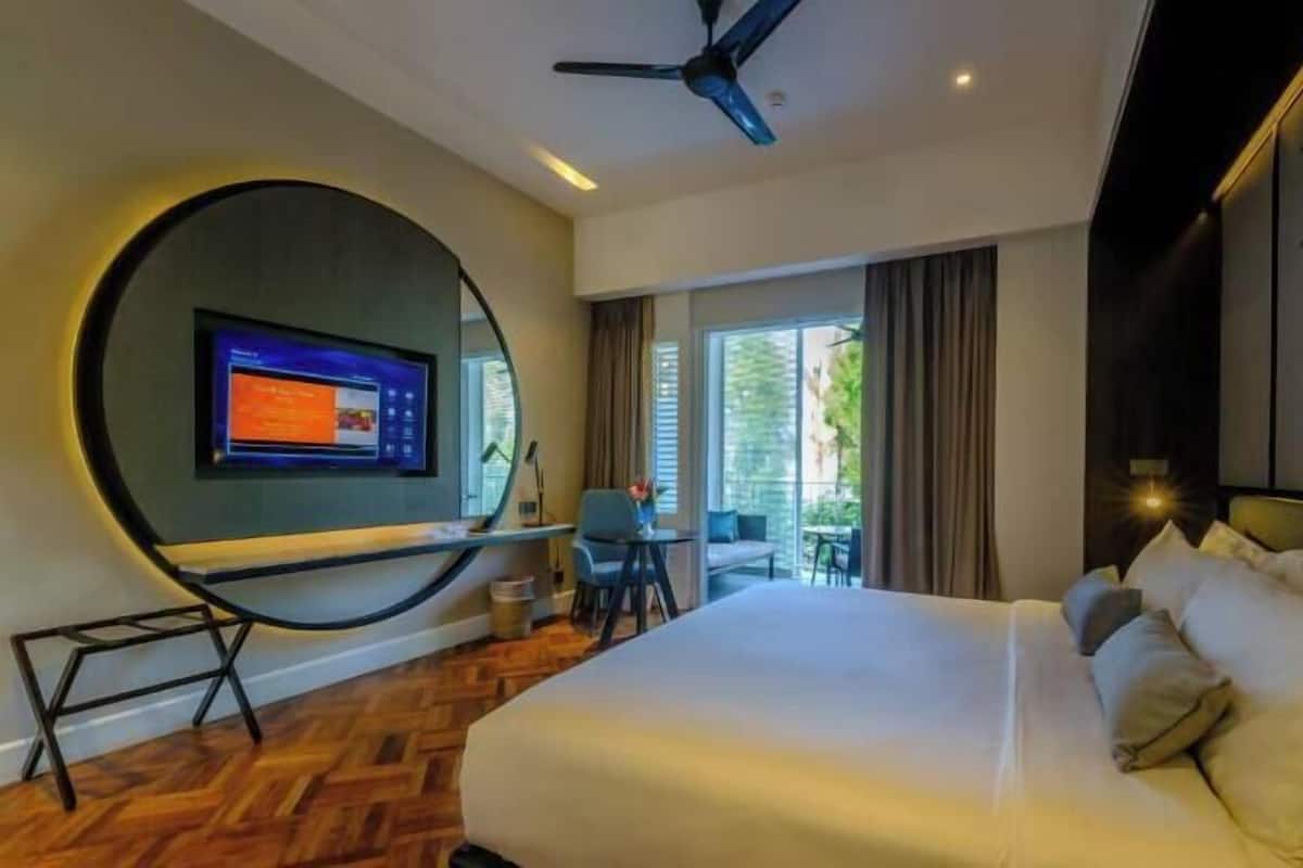 Une chambre d’hôtel avec un lit, un bureau équipé d’un ordinateur, une chaise et une grande fenêtre.