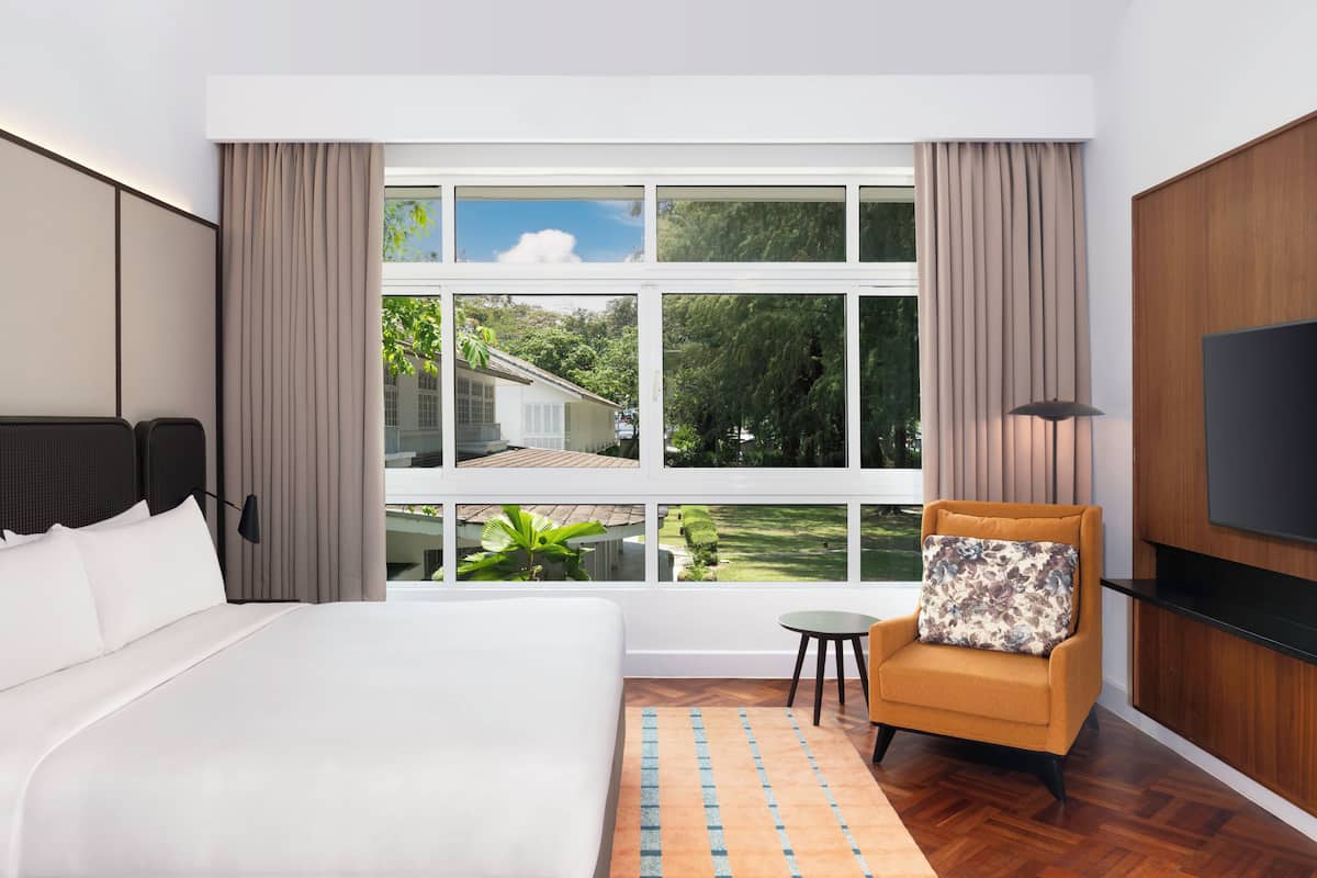 Une chambre d’hôtel avec un grand lit, une petite table, une chaise, un téléviseur et une fenêtre donnant sur un paysage verdoyant et une maison.