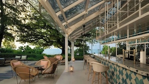 Een terras buiten met rieten meubels, een bar met krukken en uitzicht op zee.