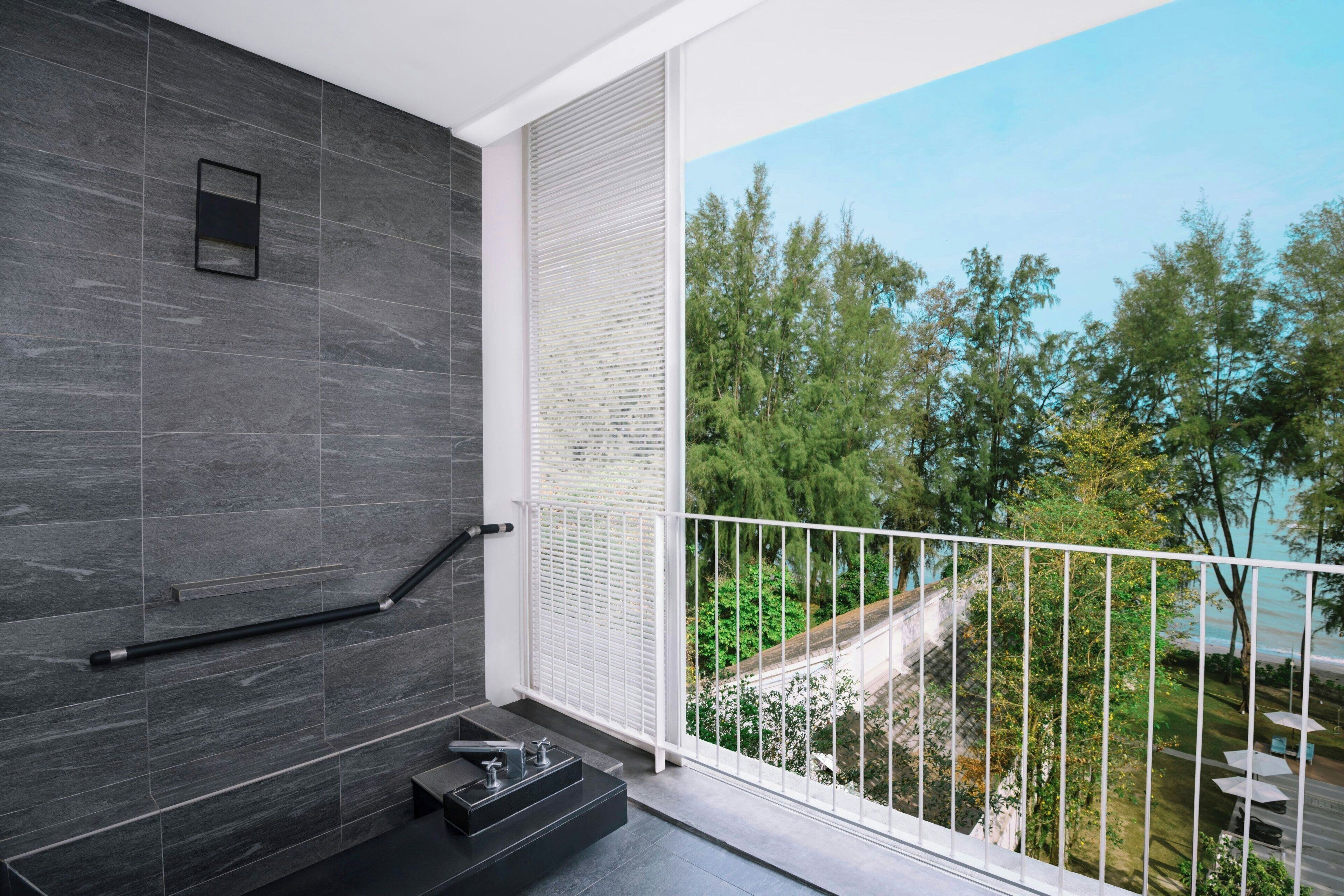 A modern bathroom with dark tiles, a black sink, and a view of a balcony with trees and a road.