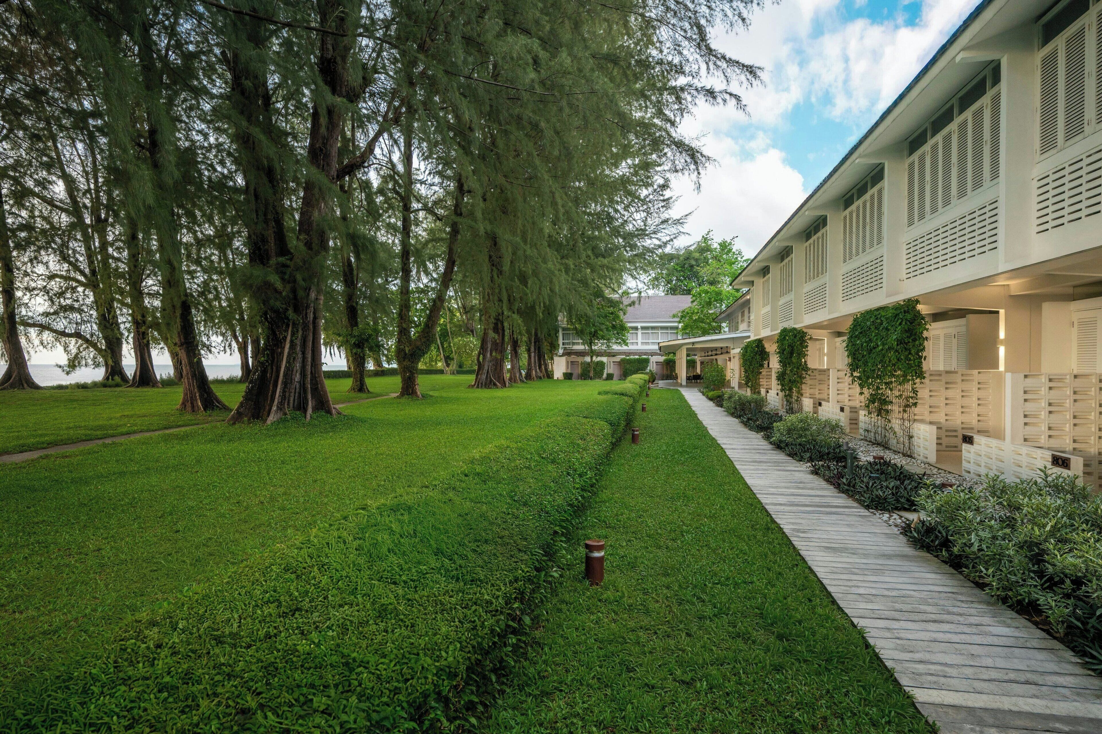 A well-maintained grassy area with a pathway leading to a building with multiple windows and a row of plants along the side.