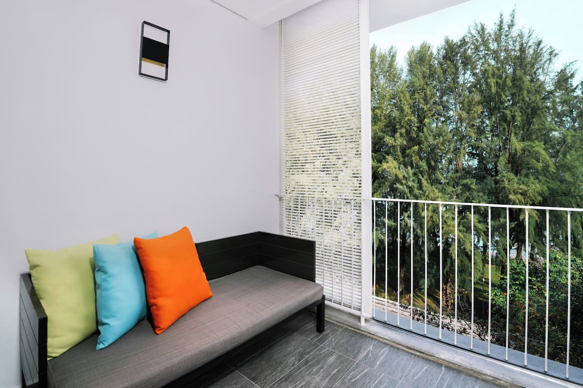 Un balcon avec un canapé gris, trois coussins de couleurs différentes et une rambarde blanche.
