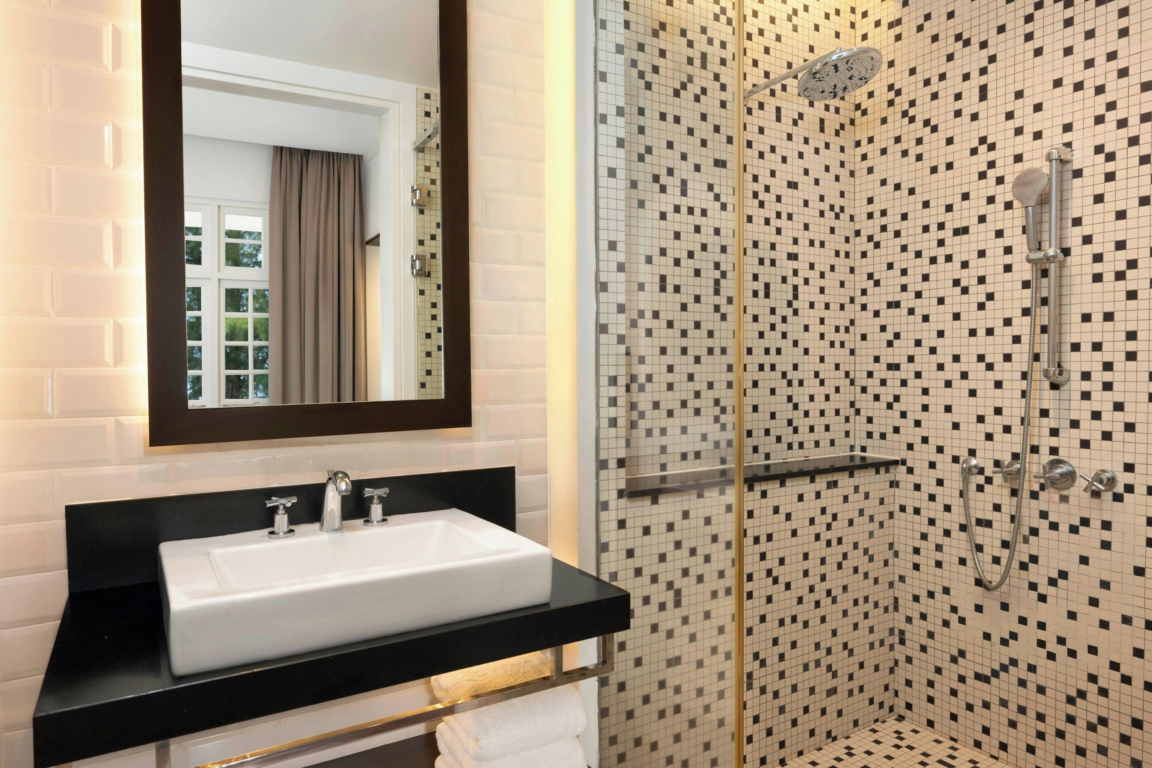 A bathroom with a white sink, a mirror, and a shower with a tiled wall.