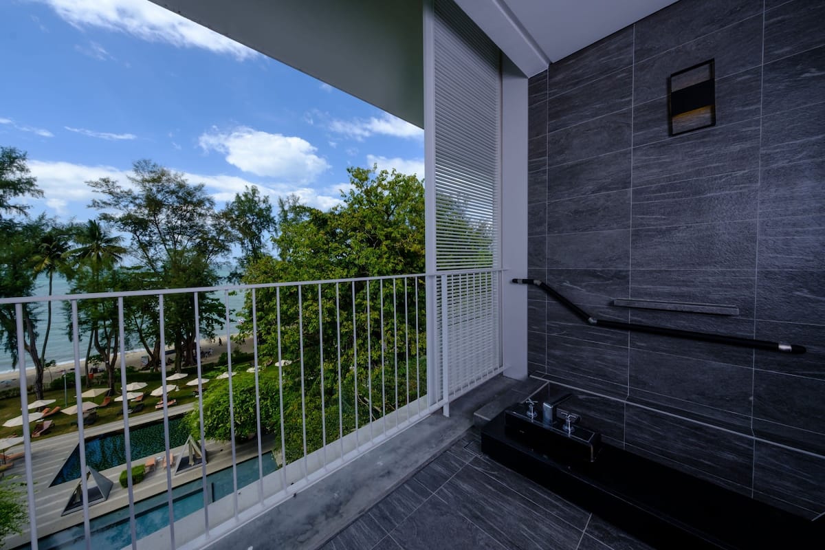 Un balcon avec une piscine, une vue sur la plage et un intérieur moderne avec des carreaux foncés et une petite fenêtre.