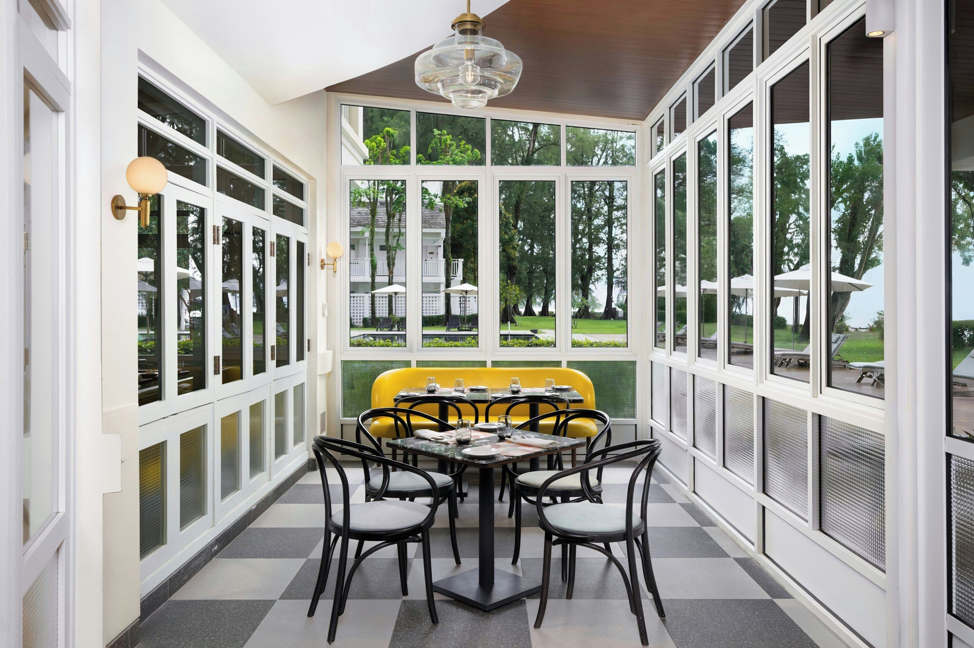 A dining area with a table and chairs, large windows, and a yellow bench.