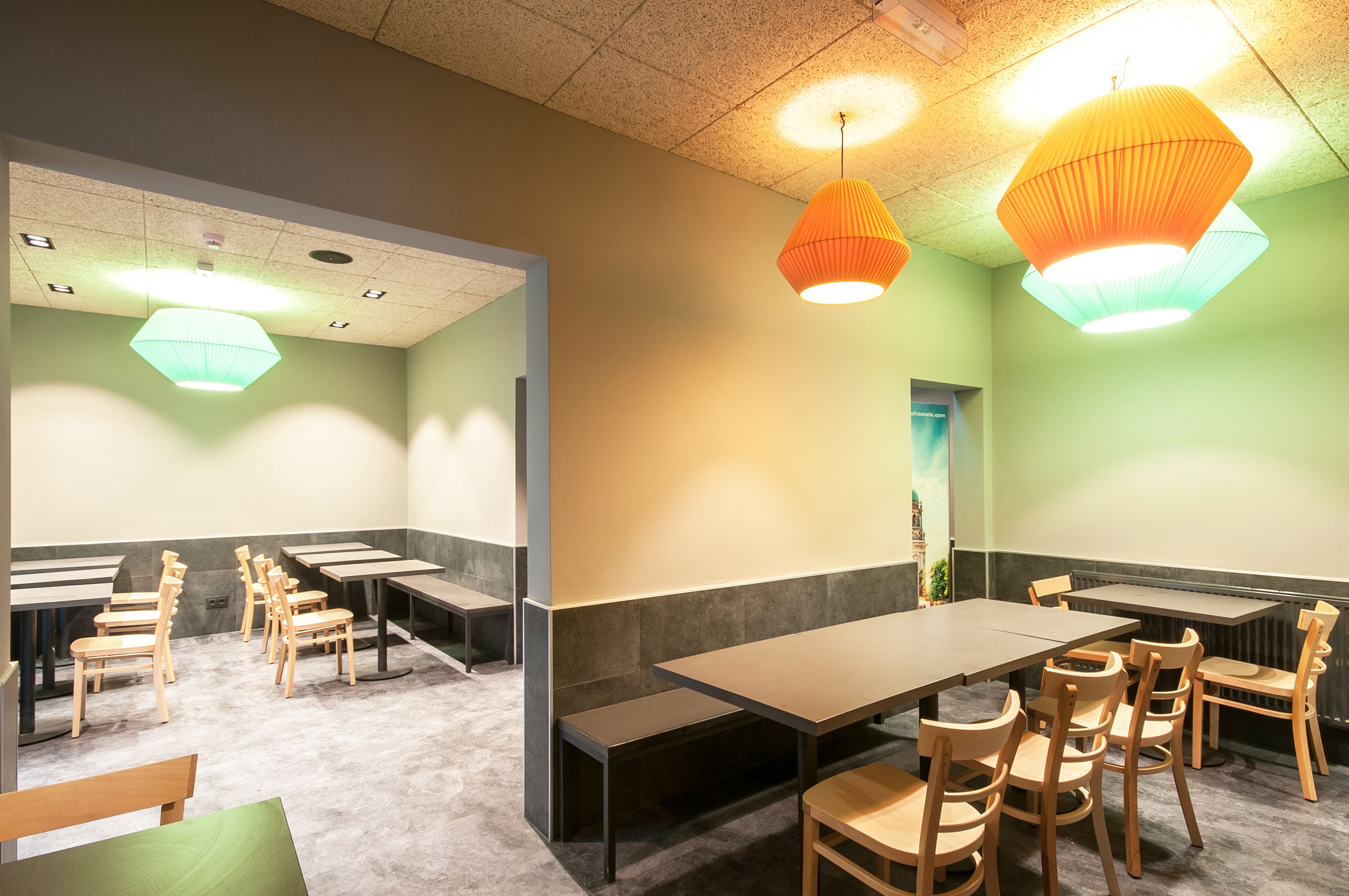A restaurant with booths and tables, wooden chairs, and pendant lighting.