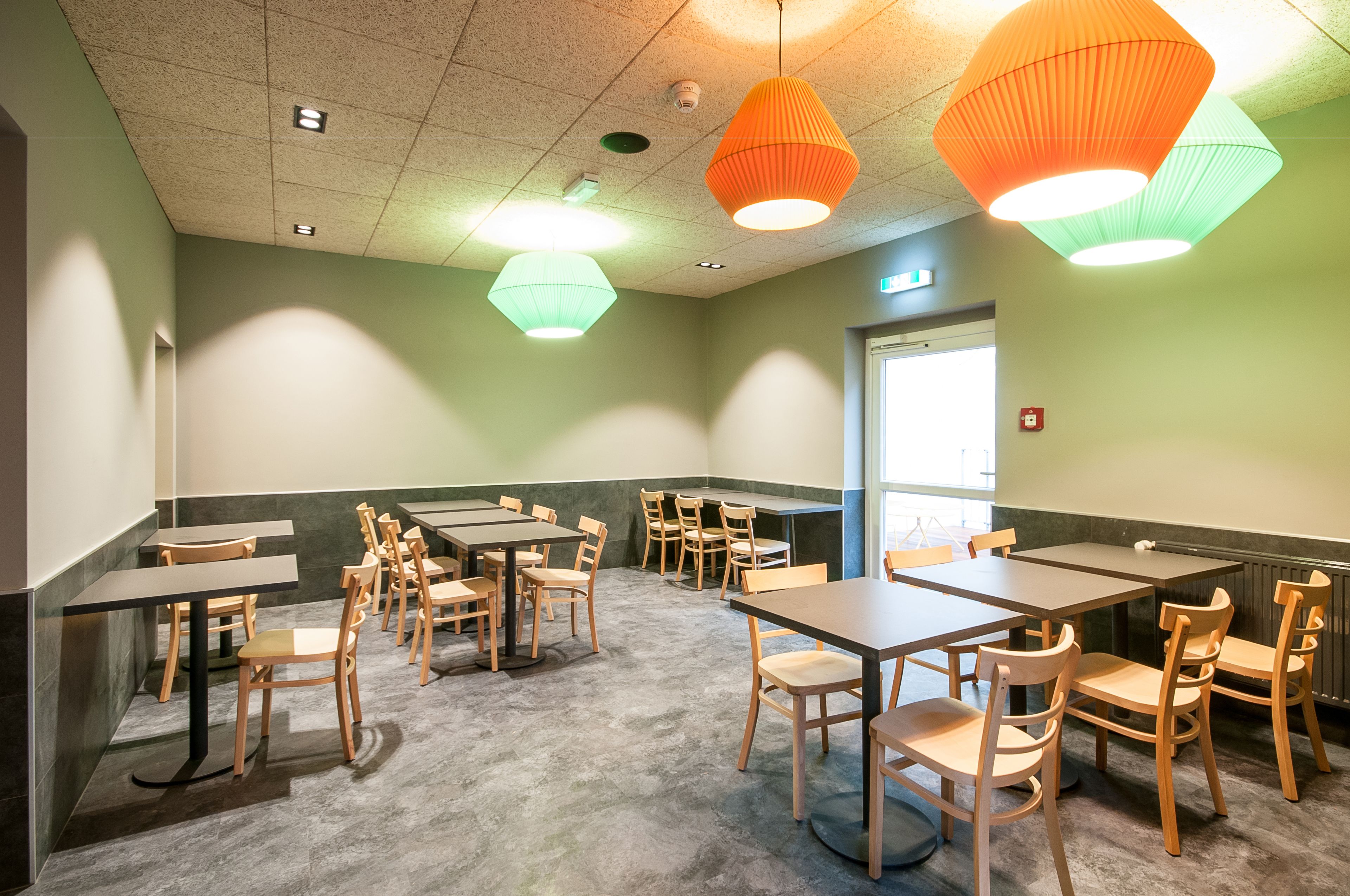 Un salón de conferencias con varias mesas y sillas, luces en el techo y una puerta.