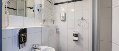 Baño con lavamanos blanco, inodoro, secamanos, espejo y dispensador de toallas.