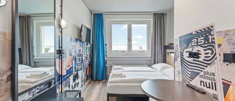 Habitación de hotel con cama, escritorio, espejo, ventana con cortinas y un cartel en la pared.
