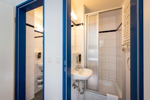 A modern bathroom with a white sink, a glass shower enclosure, and a blue door frame. - a&o Berlin Mitte (Berlin)