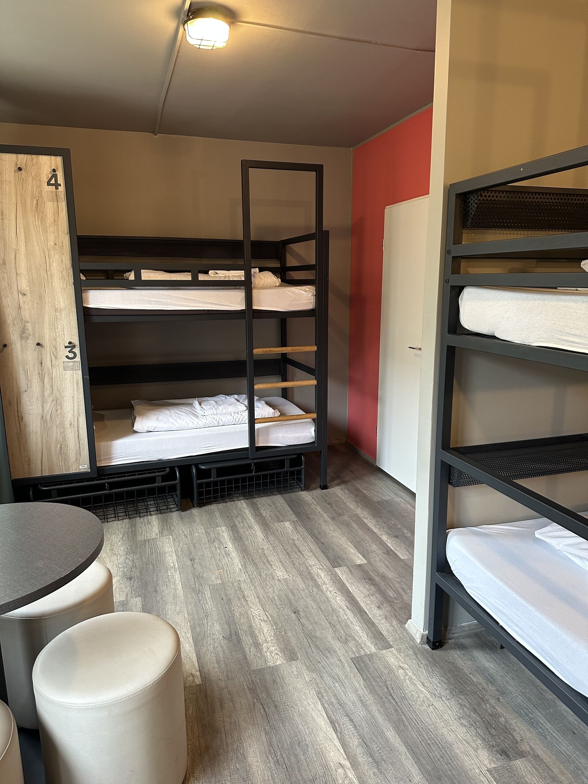 Habitación con literas, un armario de madera, una mesa redonda y dos otomanas.