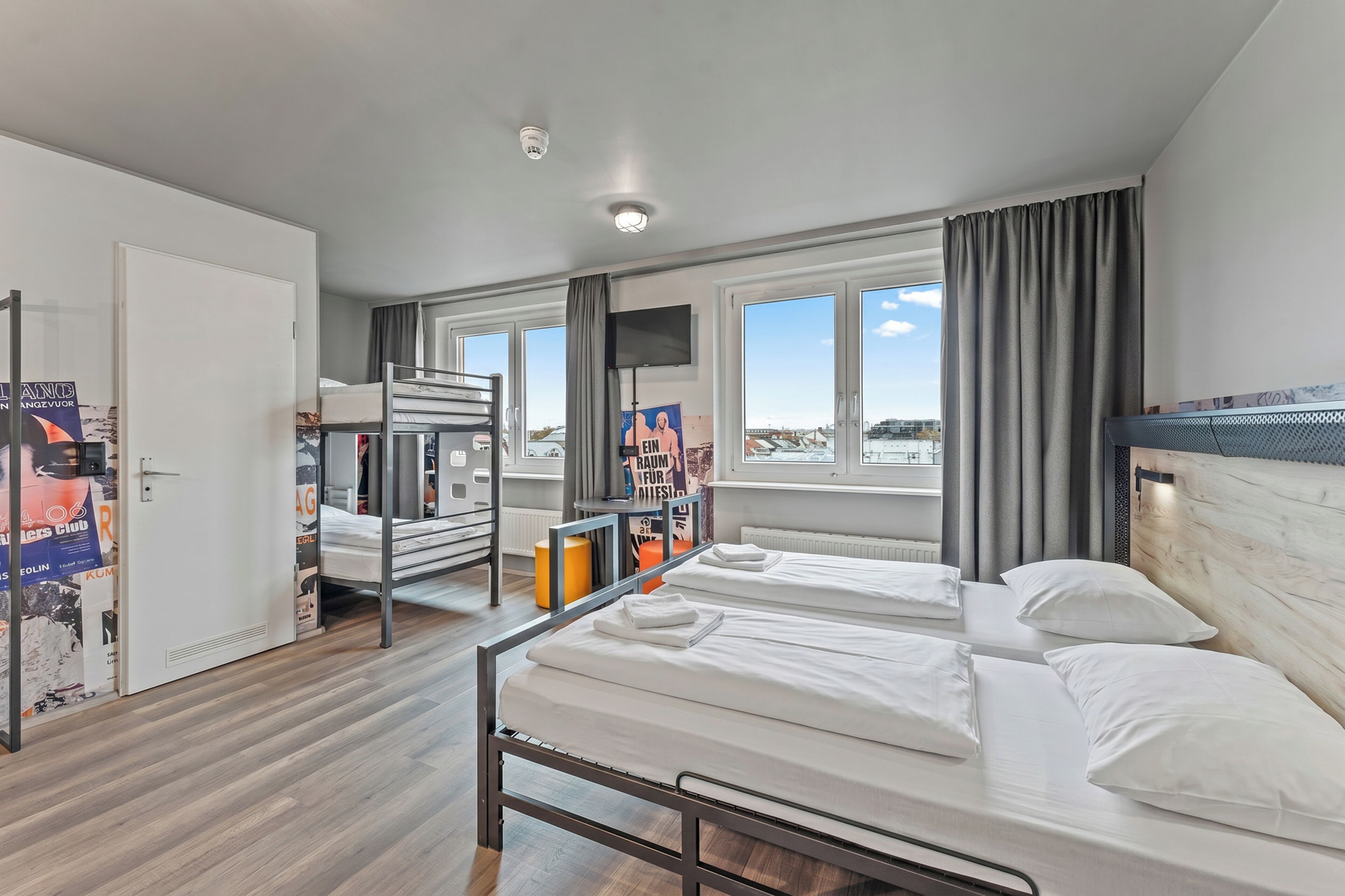A hotel room with a bunk bed, a desk, a chair, a window with a view, and a television.