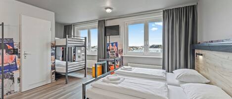 A hotel room with a bunk bed, a desk, a chair, a window with a view, and a television.