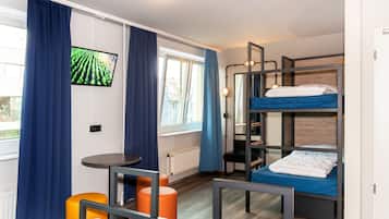 Une chambre avec des lits superposés, une télévision, une table et une fenêtre avec des rideaux.
