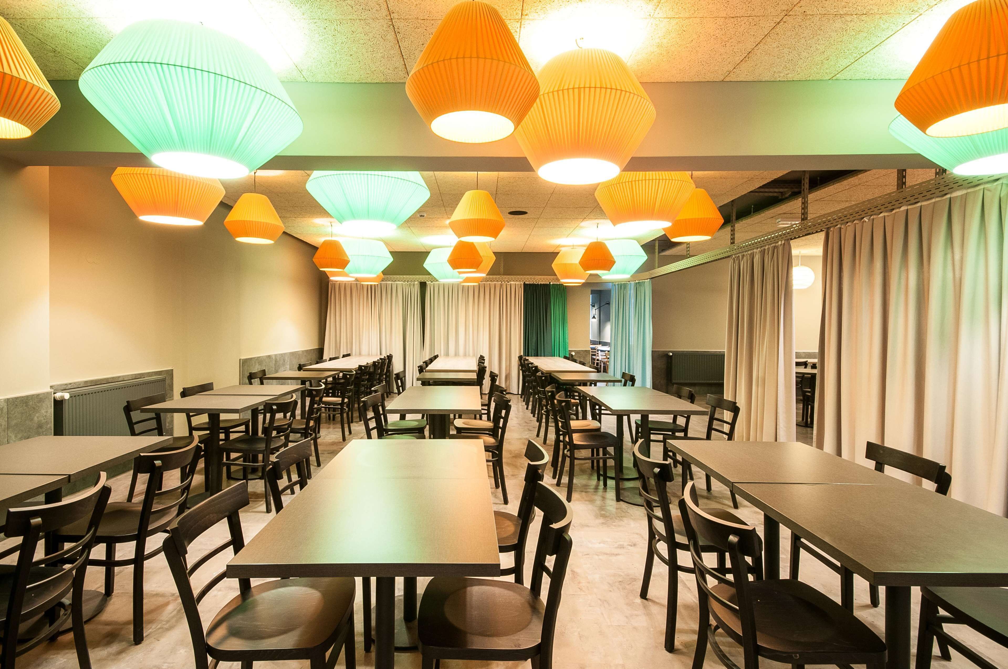 A spacious dining area with multiple tables and chairs, featuring a modern ceiling design with geometric light fixtures.