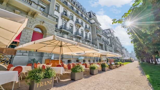 A courtyard with outdoor seating, a building with balconies, and a clear sky. - Grand Hotel National (Lucerne)
