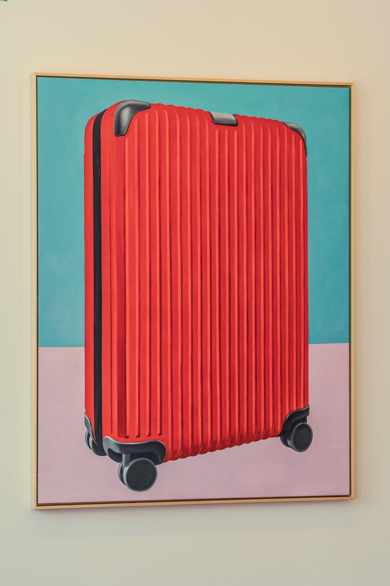 A framed painting of a red suitcase with wheels.