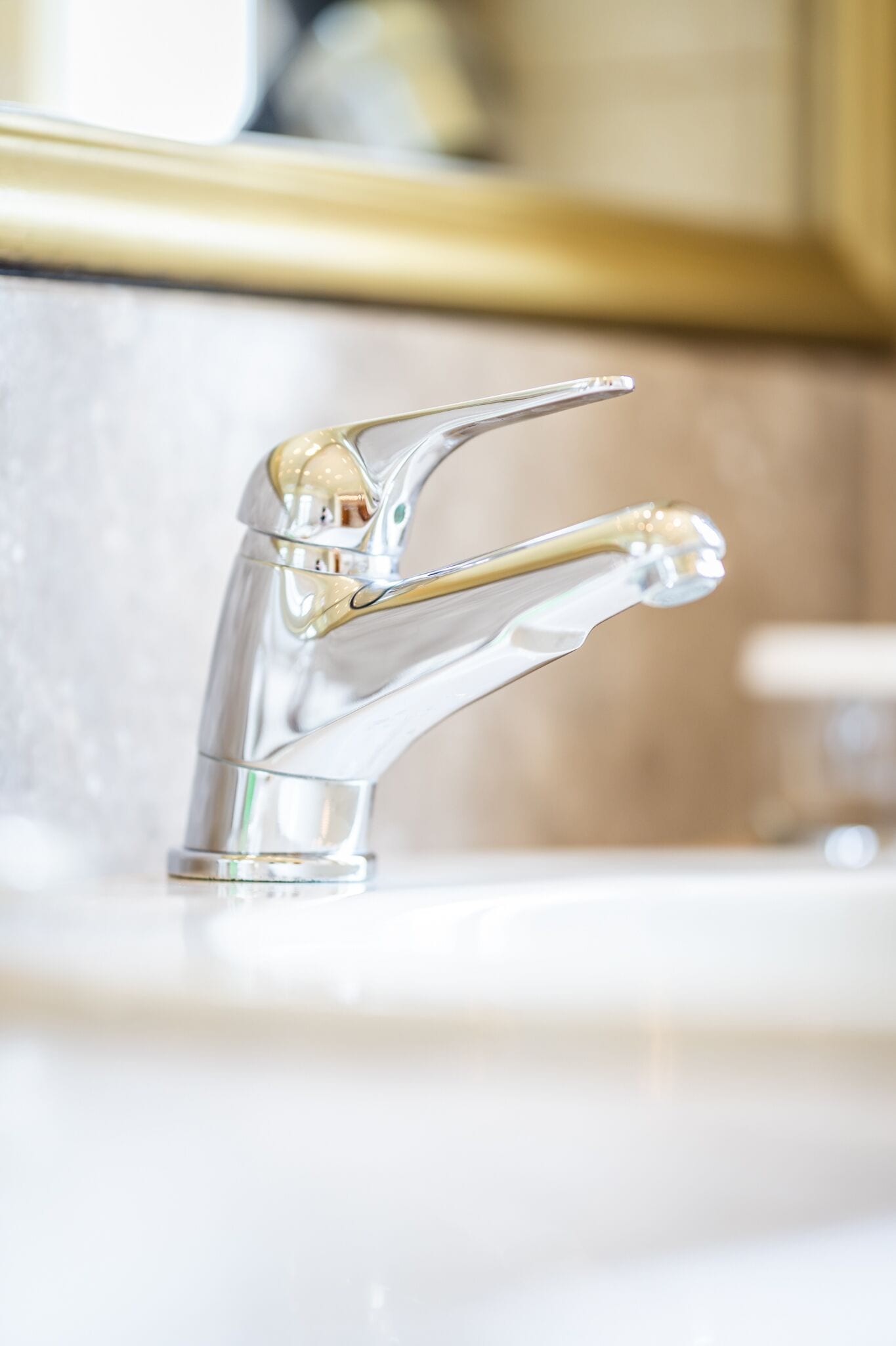A modern bathroom with a chrome faucet and a gold-colored countertop.