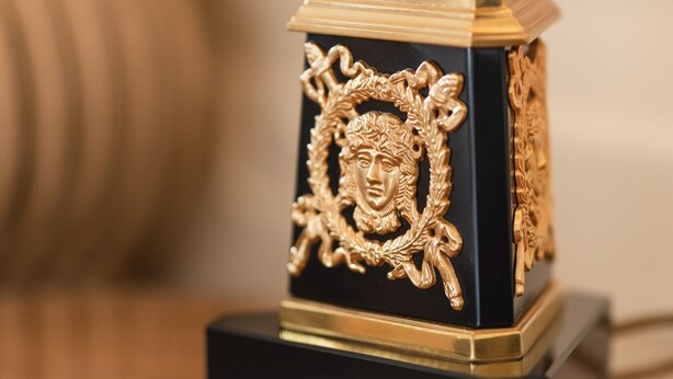 Un objeto decorativo negro y dorado con diseños intrincados sobre una superficie reflectante.