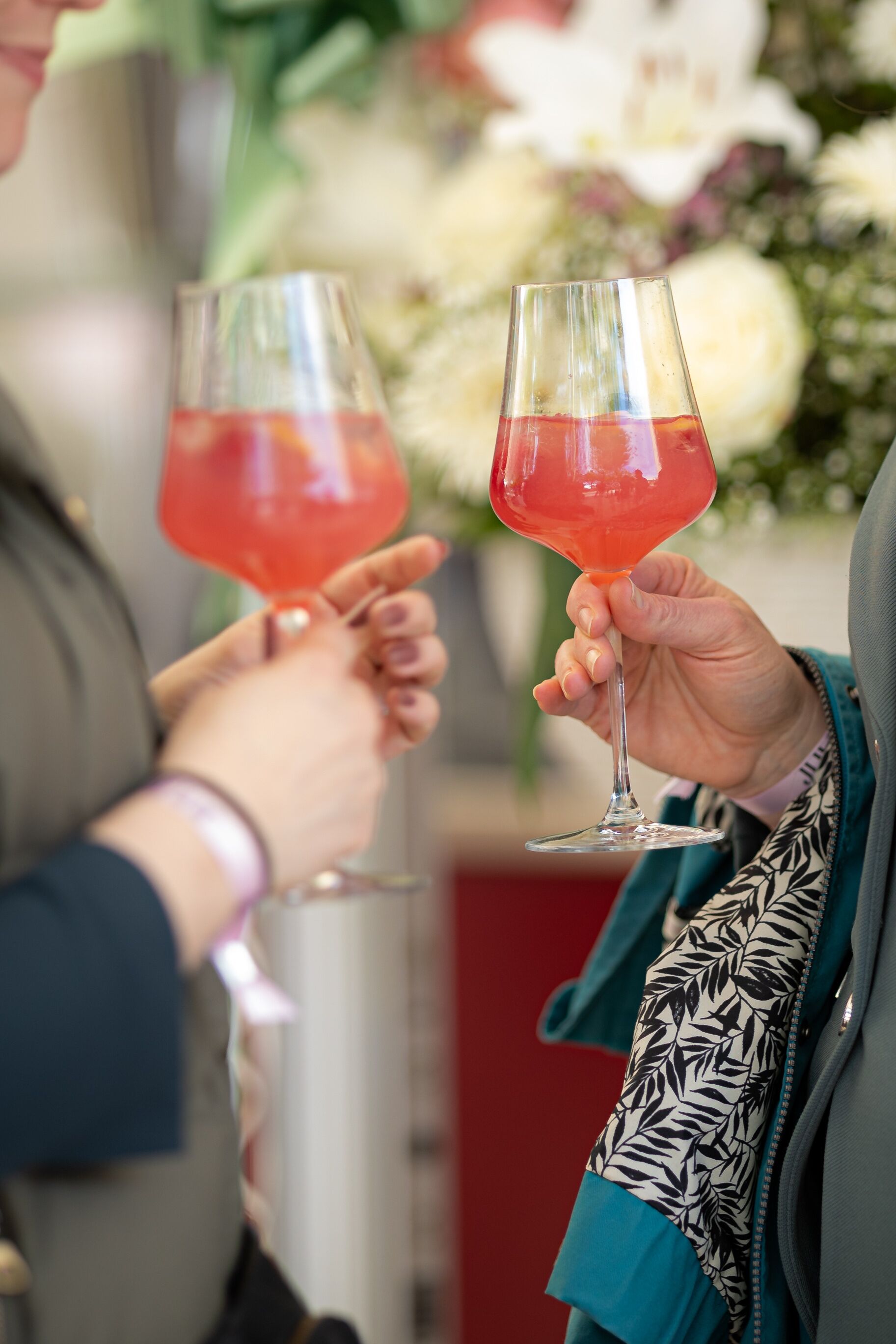 Two people holding wine glasses with a red liquid, possibly at a social event.