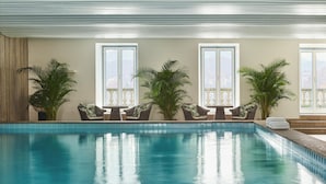 An indoor swimming pool with clear blue water, surrounded by wicker chairs and potted plants. - Grand Hotel National (Lucerne)