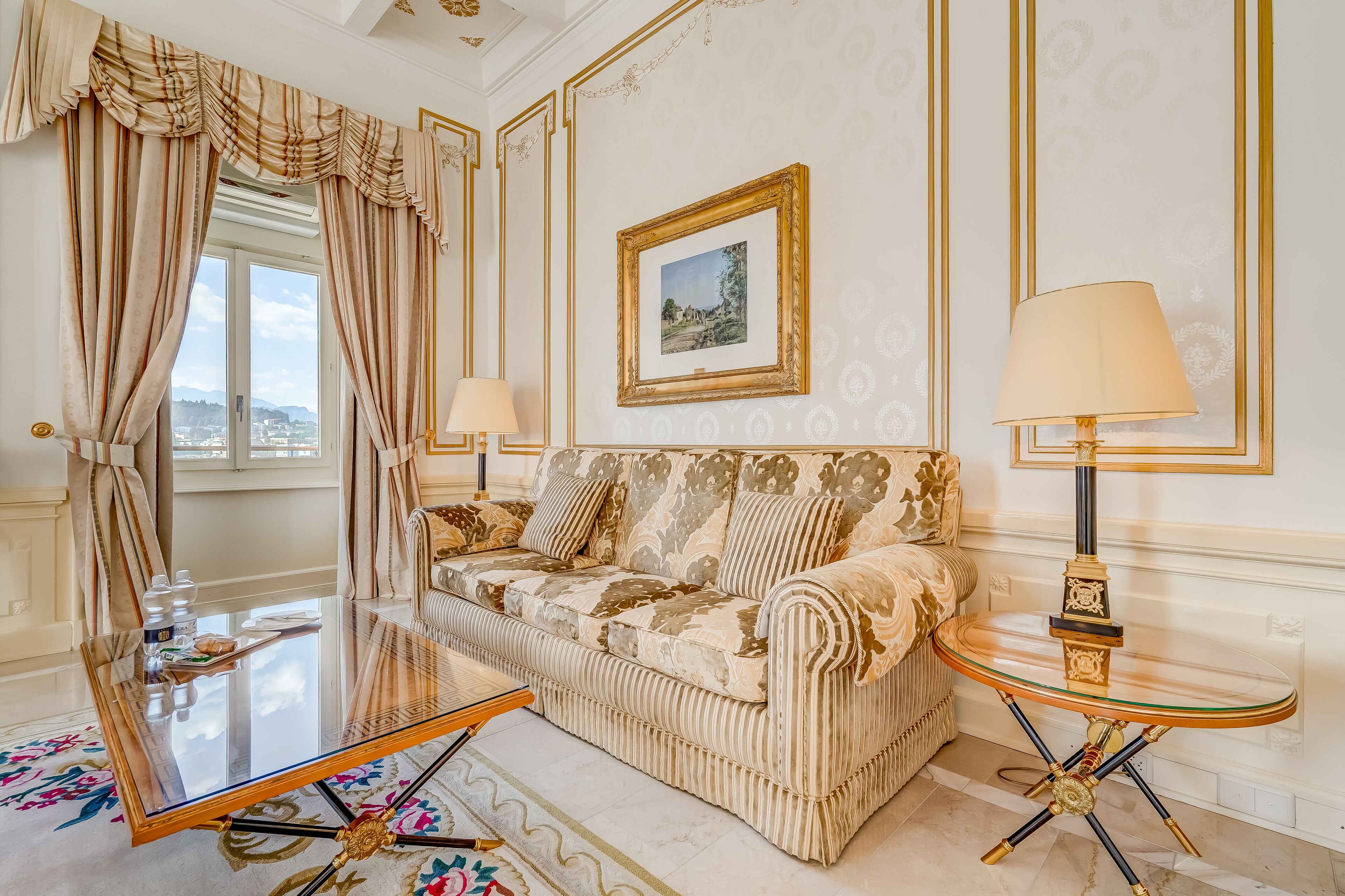 A room with a sofa, two lamps, a framed picture on the wall, and a window with curtains.