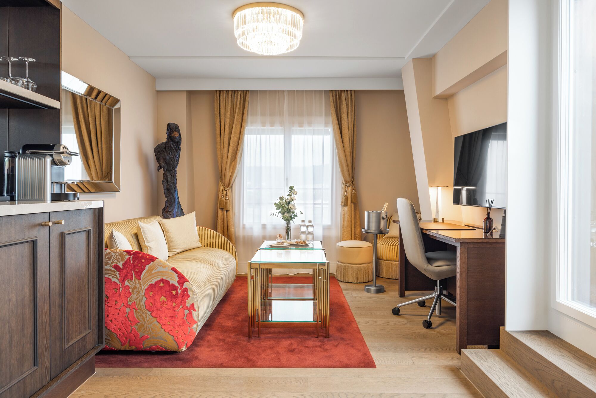 A modern living room with a sofa, a glass coffee table, a desk with a chair, and a large window with curtains.