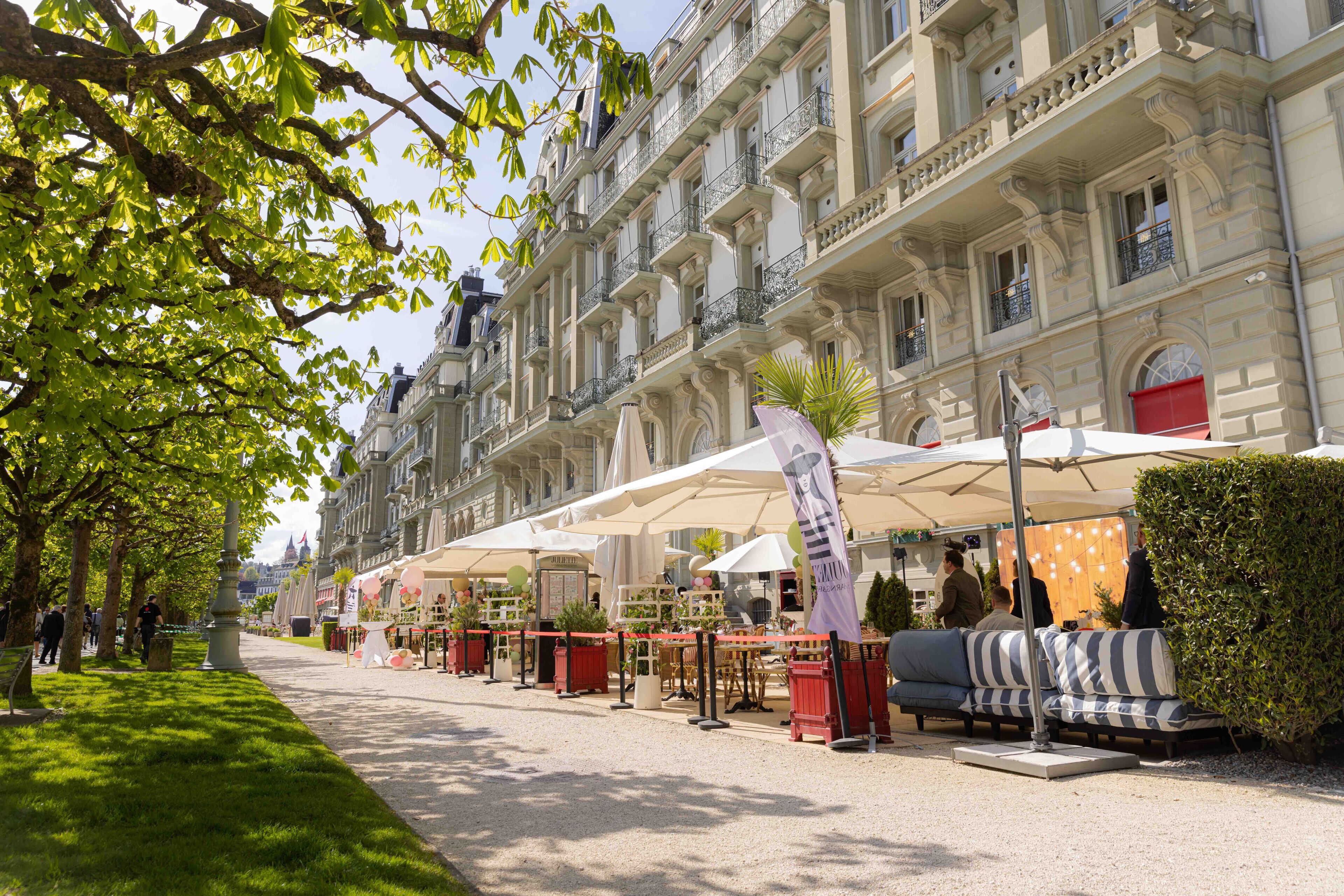 A street with outdoor seating, a building with ornate architecture, and a well-maintained lawn.
