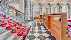 A grand staircase with ornate railings and red carpeted steps, leading to a checkered floor and a wooden reception desk. - Grand Hotel National (Lucerne)