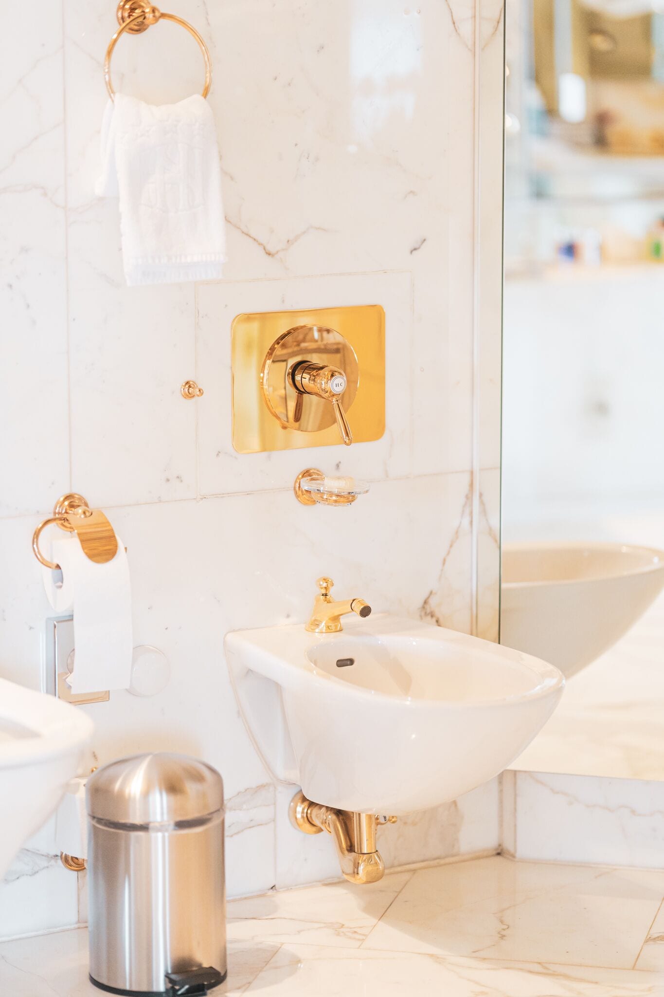 Baño con lavamanos blanco, detalles dorados y frontis de mármol.