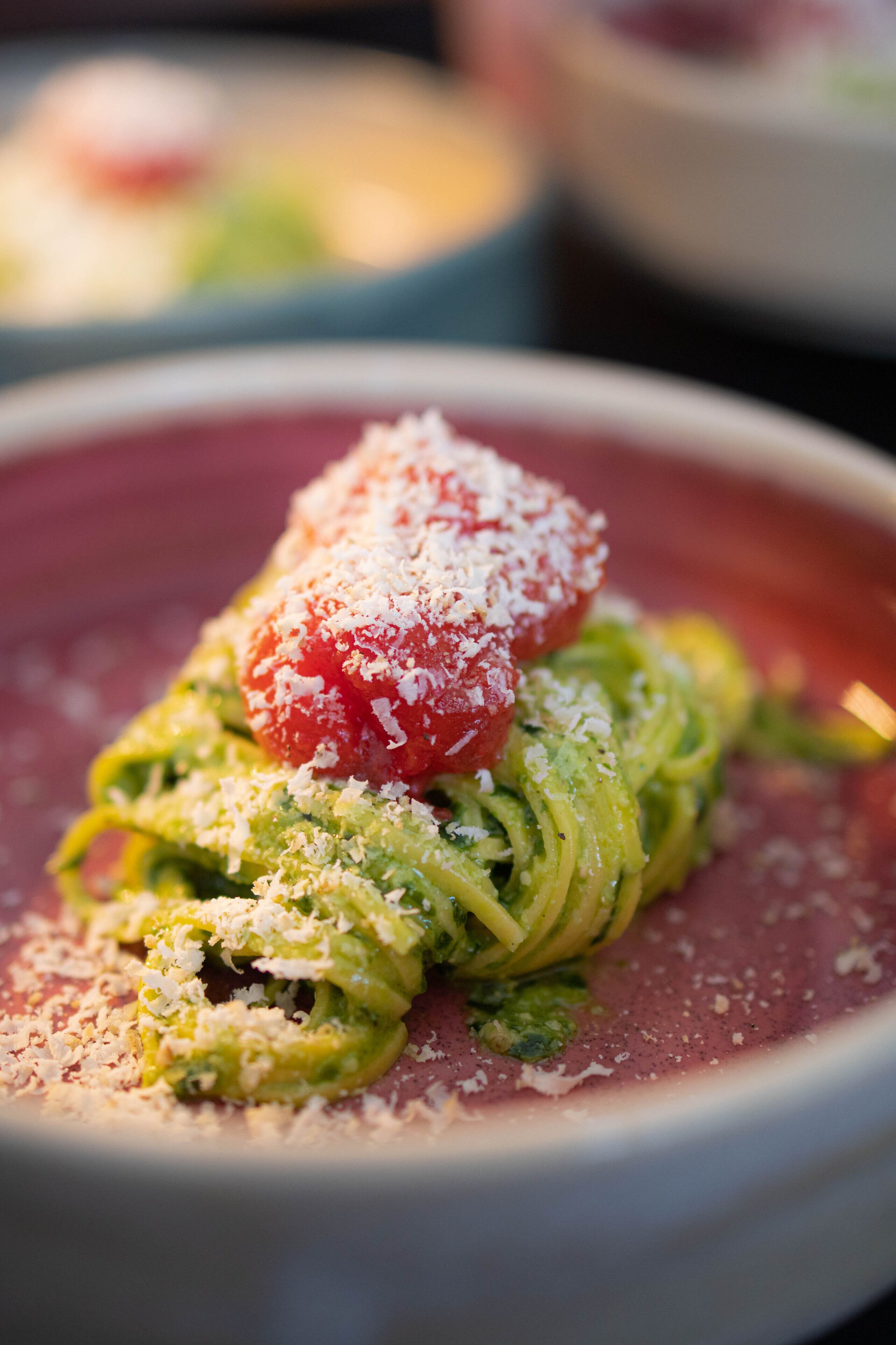 A plate of pasta with a cherry tomato and grated cheese on top.