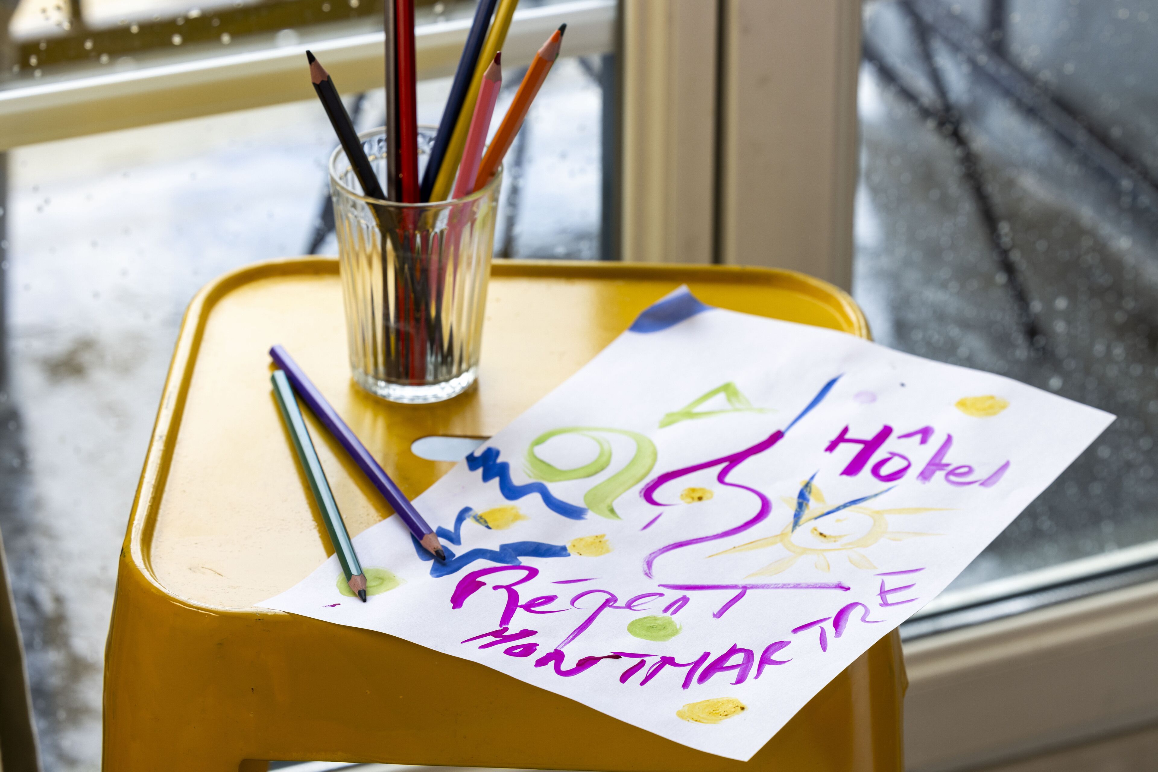 Un taburete amarillo con un vaso que contiene lápices y un pedazo de papel con escritura colorida.