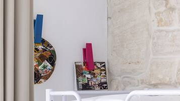 A room with a bed, a wall-mounted magazine rack, and a textured stone wall.
