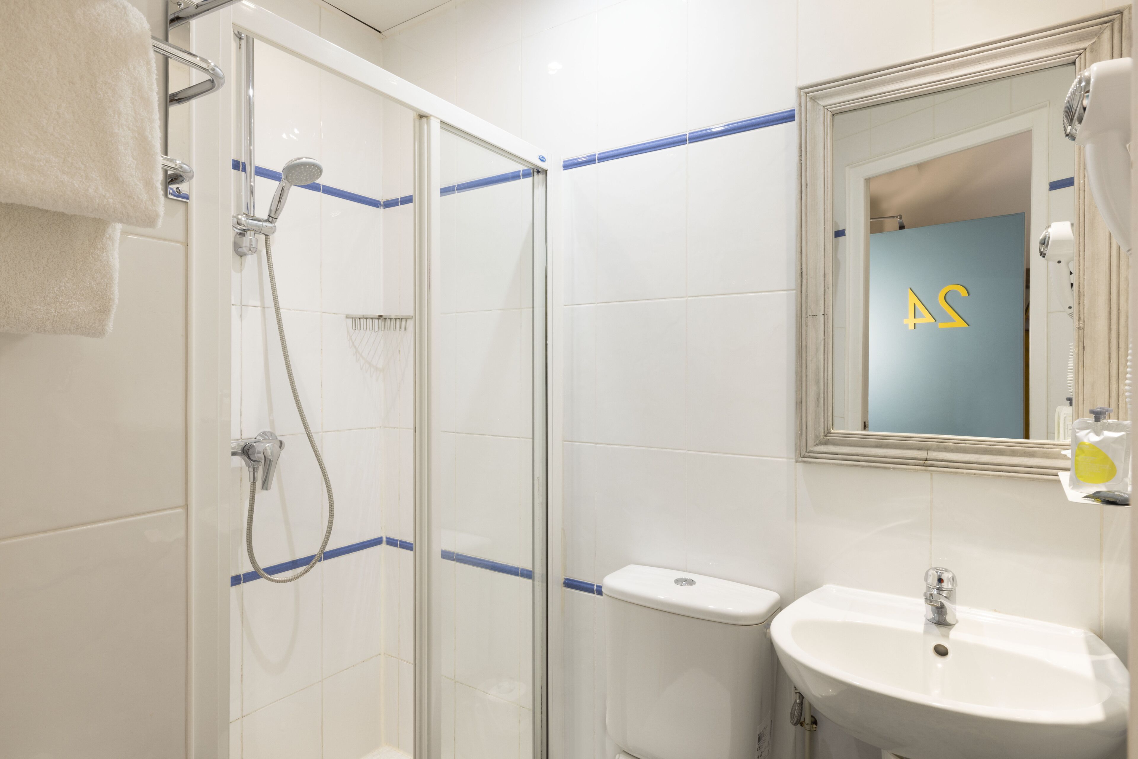 A bathroom with a glass shower enclosure, a white sink, and a mirror with a reflection of a blue door.