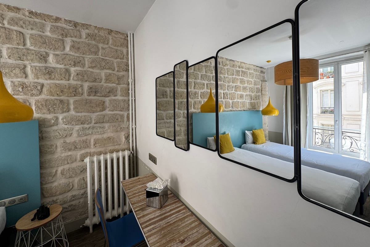 Een moderne kamer met een stenen muur, een bed met blauwe en gele beddengoed, een houten tafel met een zakdoekendoos, en een radiator.