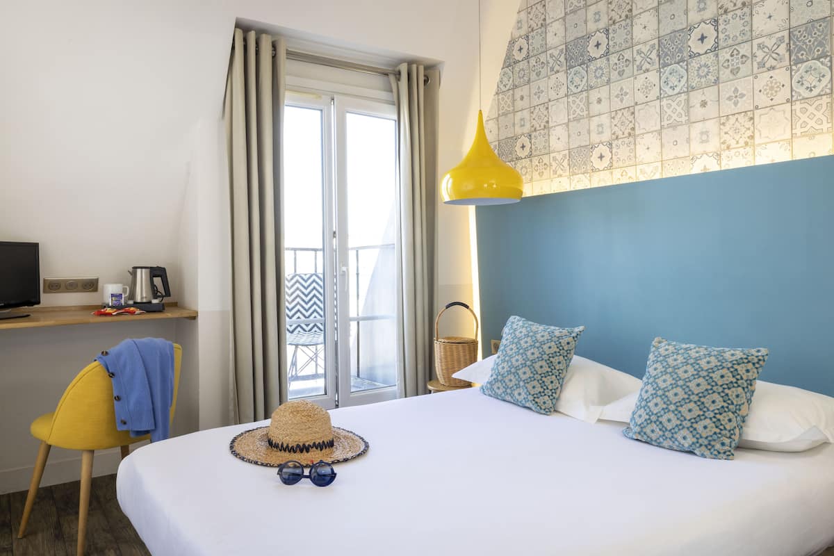 Hotelkamer met een bed, een bureau met computer, een stoel, een raam met gordijnen en een behang met een patroon.